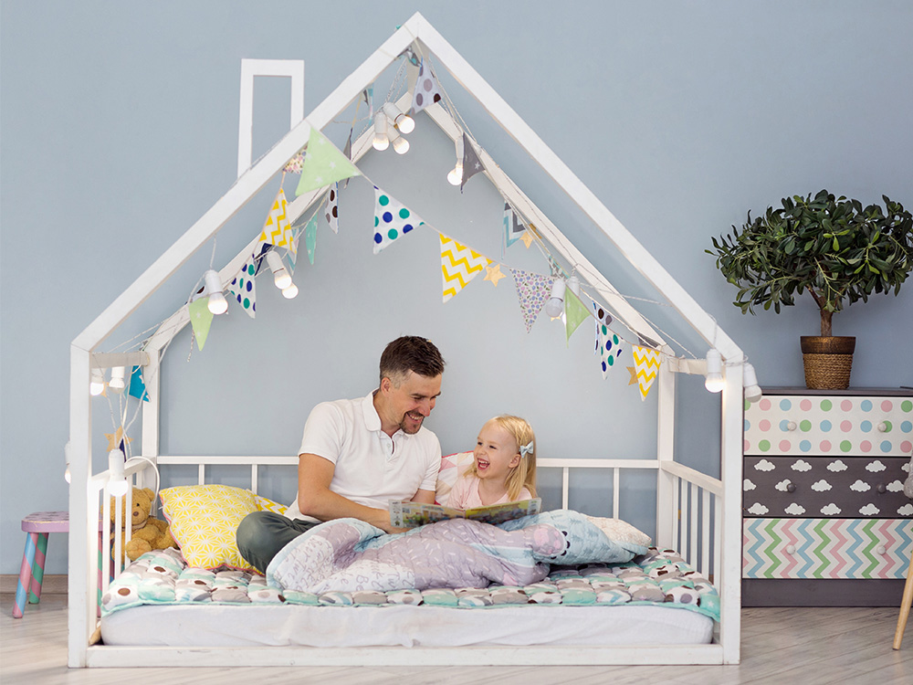 um pai brincando com uma menina na cama de uma casa